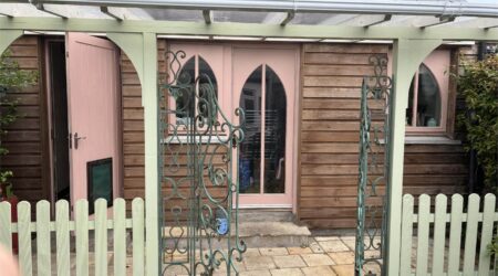 External baby pink and natural wood cottage shed extension with wood and metal fencing - before image.