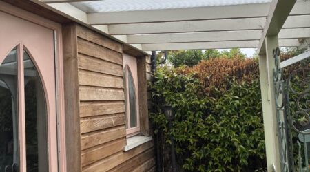 External baby pink and natural wood cottage shed extension with wood and metal fencing - before image.