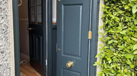 Exterior after painting photo of a dark green front door with gold fixtures opening into house by Cornelius Green Decorators